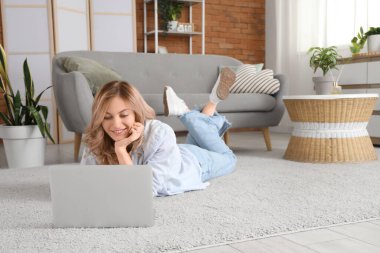 Evdeki halıda dizüstü bilgisayar kullanan güzel bir kadın.
