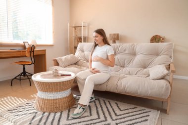 Gebelik diyabeti ve glikoz sensörü olan hamile bir kadın evdeki kanepede oturuyor.