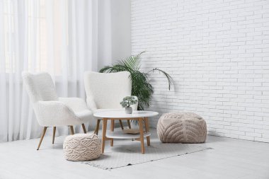 Koltuklar, kahve masası ve puflar oturma odasının içinde.