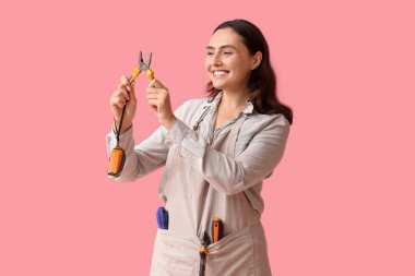 Pembe arka planda pense ve mezurası olan genç bir inşaat işçisi. Erkek mesleği kavramındaki kadın.