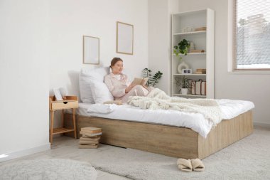 Pijamalı, evde kitap okuyan güzel, genç ve mutlu bir kadın.