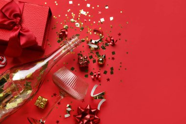 Şampanya şişesi, konfeti, bardak ve kırmızı arka planda hediye. Yeni yıl kutlaması