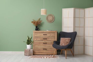 Çekmeceler, katlanan ekran ve yeşil duvarın yanındaki koltuk.