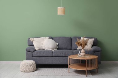 Konforlu kanepe ve yeşil duvarın yanındaki vazoda otlar olan kahve masası.