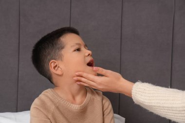 Anne yatak odasında hasta oğlunun boğazını kontrol ediyor, yakın plan.