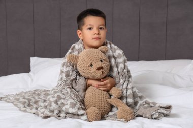 Boğazı ağrıyan küçük Asyalı çocuk ve yatak odasında oturan oyuncak ayı.