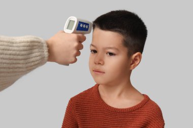 Anne, hasta oğlunun ateşini arka planda ölçüyor, yakın plan.