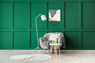 Koltuk, sehpa ve yer lambası yeşil duvarın yanında.