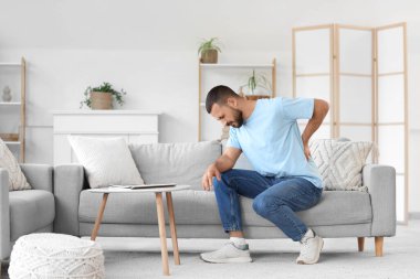 Evdeki kanepede sırt ağrısı çeken genç bir adam.