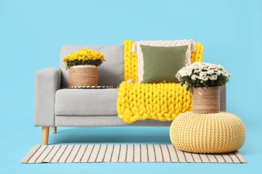 Mavi arka planda yastıklı, ekoseli ve kasımpatı çiçekli rahat bir kanepe.