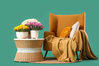 Kahve masası, yastıklı kahverengi koltuk ve yeşil arka planda kasımpatı çiçekleri.