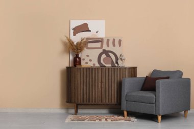 Gri koltuk ve çekmeceler. Odada kahverengi duvarın yanında resimler var.