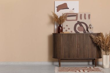 Çekmeceler, vazodaki otlar ve odadaki kahverengi duvarın yanındaki resimler.