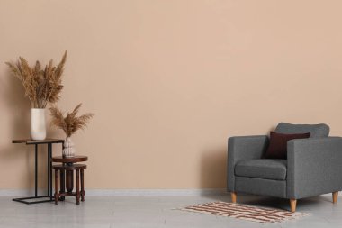 Kahverengi duvarın yanındaki vazolarda gri koltuk ve pampalar var.