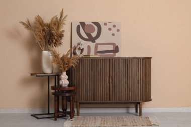 Çekmeceler, vazodaki otlar ve odadaki kahverengi duvarın yanındaki resim.