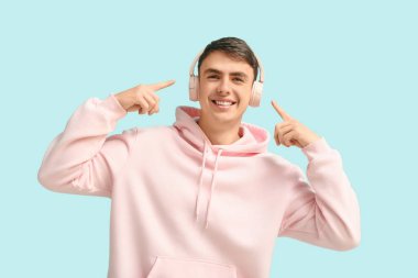 Yakışıklı genç adam mavi arka plandaki kulaklıklarına işaret ediyor.