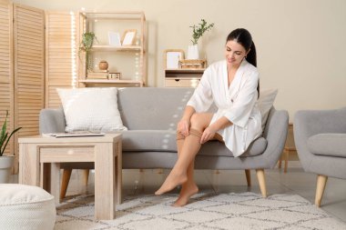 Genç kadın kanepede otururken tayt giyiyor.