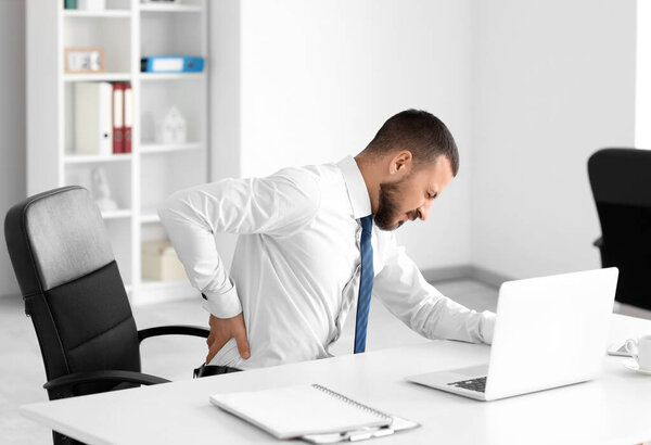 Young businessman suffering from back pain at table in office