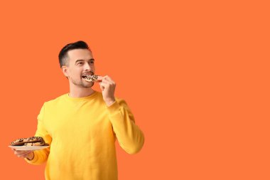 Yakışıklı adam turuncu arka planda lezzetli kurabiyeler yiyor.
