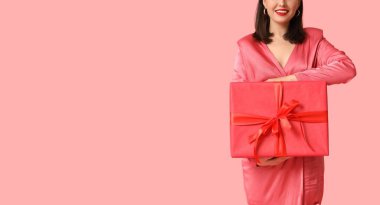 Genç, mutlu bir kadın pembe arka planda hediye kutusu tutuyor ve mesaj için yeri var. Sevgililer Günü kutlaması