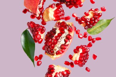 Tohumları ve yaprakları eflatun arkaplanda uçuşan taze narlar.