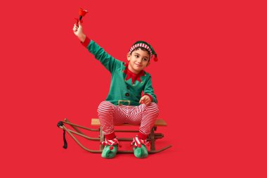 Kızaklı şirin bir elf ve kırmızı arka planda Noel çanı.