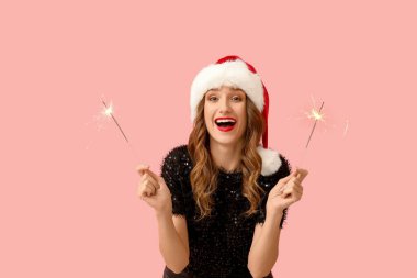 Pembe arka planda maytapları olan Noel Baba şapkalı mutlu bir genç kadın.