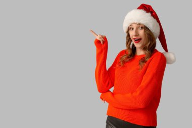 Noel Baba şapkalı genç kadın gri arka planda bir şeye bakıyor.