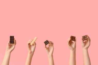 Pembe arka planda farklı tatlı çikolataları olan kadın elleri.