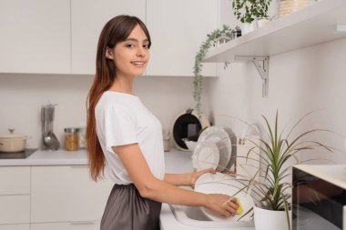 Genç bir kadın mutfakta bulaşık yıkıyor.