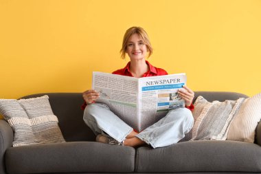 Evdeki kanepede gazete okuyan güzel bir genç bayan.