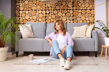 Elinde gazete ve bir fincan çayla evdeki kanepenin yanında oturan genç ve güzel bir kadın.