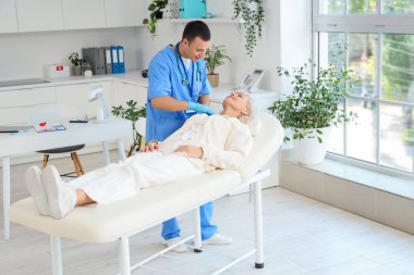 Erkek endokrinolojist klinikteki kanepede tiroit bezini inceliyor.