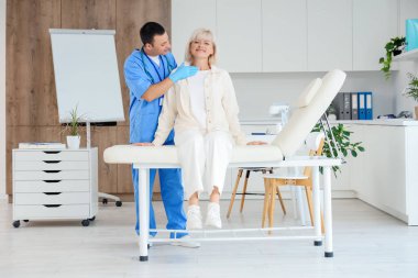 Erkek endokrinolojist klinikteki kanepede tiroit bezini inceliyor.