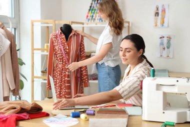 Atölyede dizüstü bilgisayarla çalışan kadın terzi.