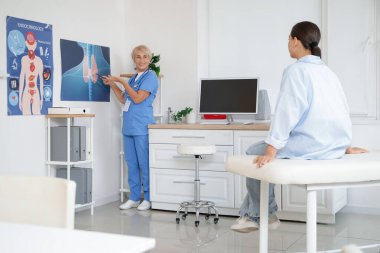 Kadın endokrinolog tiroit bezinin resmini klinikteki hastaya gösteriyor.