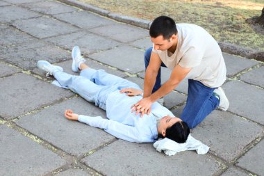 Genç adam kalp masajı yapıyor. Baygın karısı parkta kalp krizi geçiriyor.