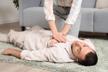 Genç bir kadın evde kalp krizi geçiren baygın bir kocaya kalp masajı yapıyor.