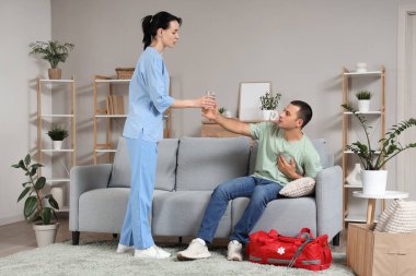 Kalp krizi geçiren genç bir adam evde doktordan bir bardak su alıyor.