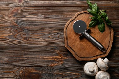 Ahşap arka planda paslanmaz çelik pizza bıçağı, fesleğen ve mantarlı tahta.
