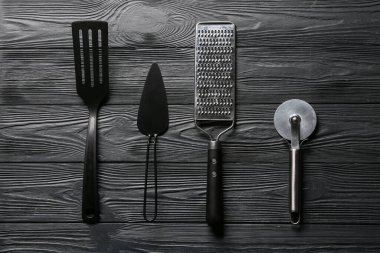 Koyu ahşap arka planda paslanmaz çelik pizza keskisi olan farklı mutfak aletleri.