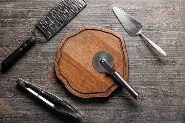 Paslanmaz çelik pizza keskisi, spatula, maşa ve ahşap kaplama rendesi olan tahta tahta.