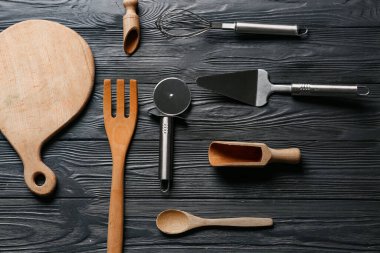 Koyu ahşap arka planda paslanmaz çelik pizza keskisi olan farklı mutfak aletleri.
