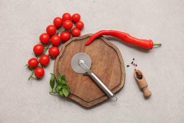 Paslanmaz çelik pizza keskisi, ahşap tahta, taze sebzeler ve arka planda baharatlar.