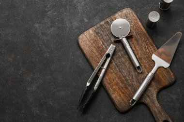 Ahşap tahta tahta, paslanmaz çelik pizza kesici, spatula, maşa ve baharatlar.