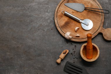 Paslanmaz çelik pizza kesicisi, spatula ve koyu arkaplanda baharatlar.
