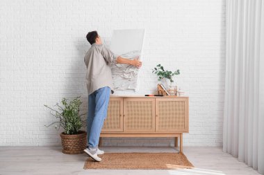 Evdeki beyaz tuğlalı duvara resim asan genç adam.