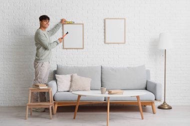 Çekiçli ve katlı genç adam oturma odasının duvarında boş bir çerçeve asılı