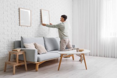 Oturma odasındaki duvarda boş bir çerçeve asılı genç adam