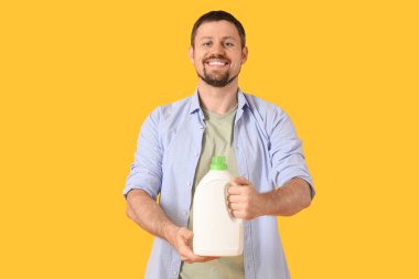 Sarı arka planda çamaşır deterjanı olan genç bir adam.